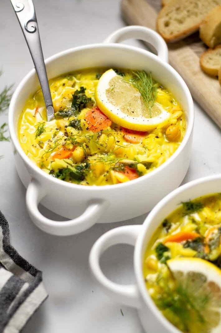 Close up shot of lemon orzo soup in a white bowl garnished with fresh dill