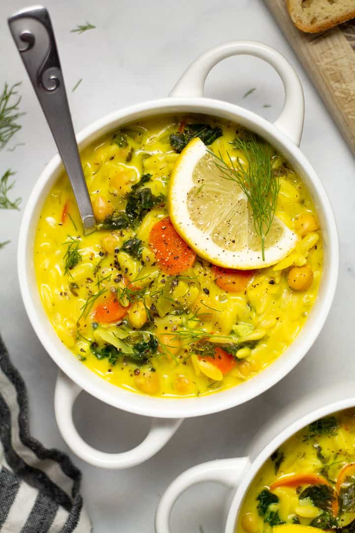 Overhead shot of lemon orzo soup in a white bowl garnished with fresh dill
