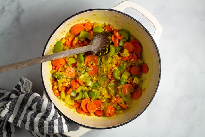 Large white dutch oven filled with vegetables and spices to make lemon orzo soup
