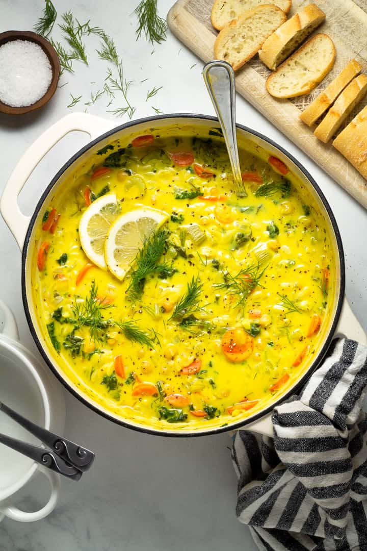 Large white dutch oven filled with creamy vegan lemon orzo soup garnished with fresh dill