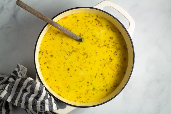 Large white dutch oven filled with creamy vegan lemon orzo soup