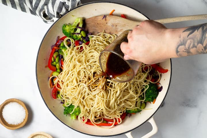 Overhead shot of stir fry sauce being added to a pan of veggie lo mein