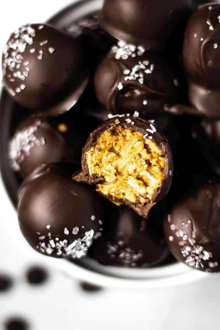 Close up shot of a white bowl filled with peanut butter balls with a bite taken out of one