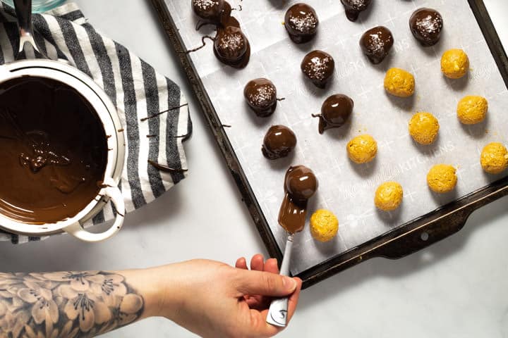 Peanut butter balls being dipped in chocolate and transferred to baking sheet 