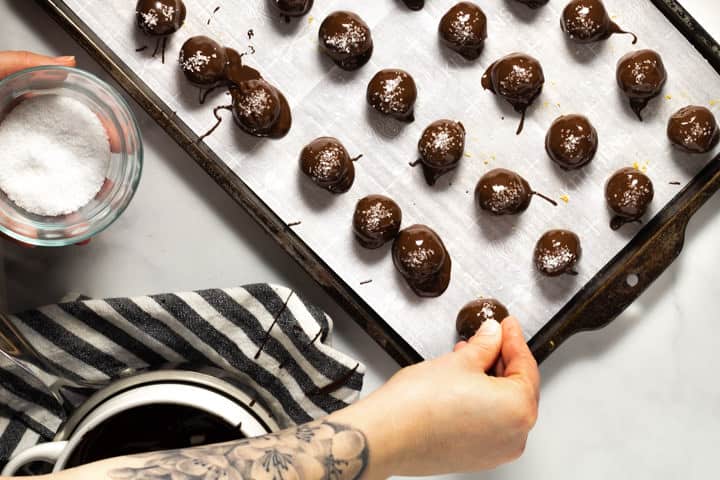 Parchment lined baking sheet with chocolate covered peanut butter balls being sprinkled with salt 