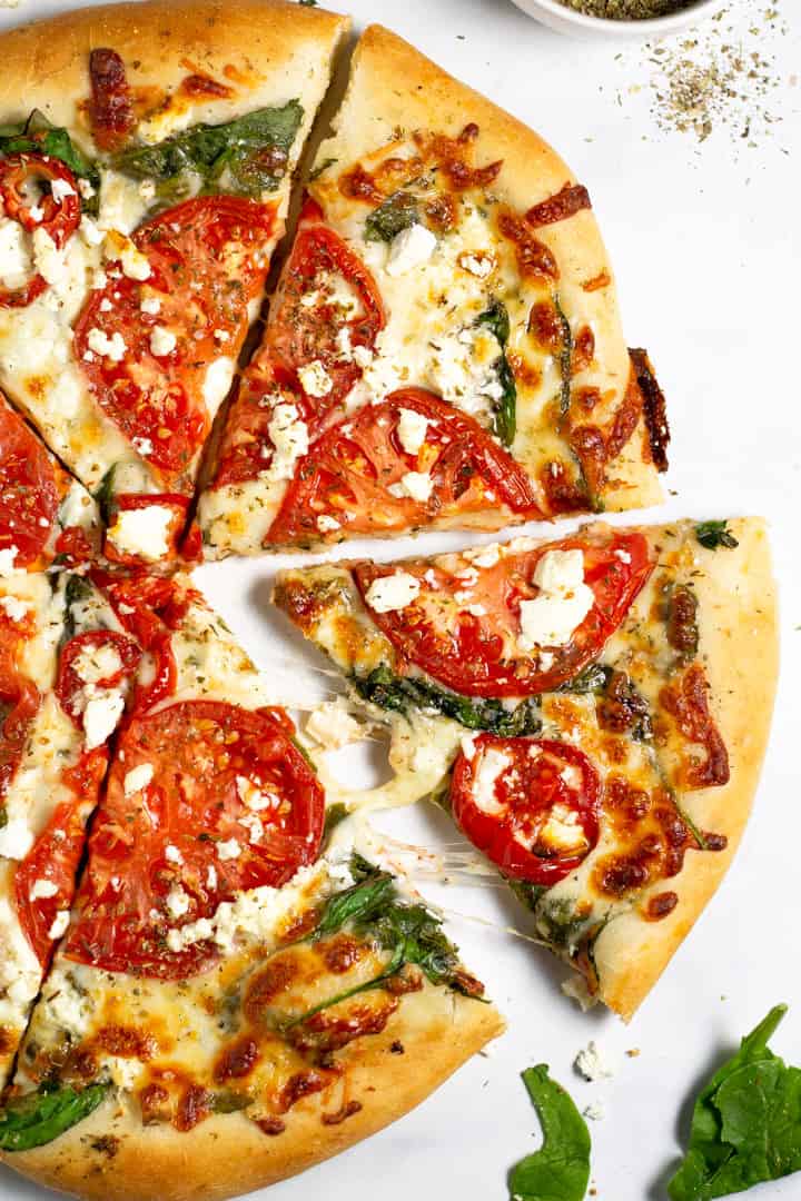 Overhead shot of a tomato pesto and spinach pizza on a white counter top 
