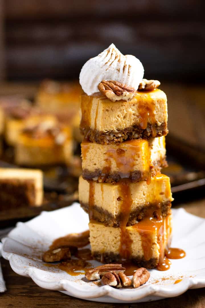 Tower of pumpkin cheesecake bars garnished with caramel and whipped cream 