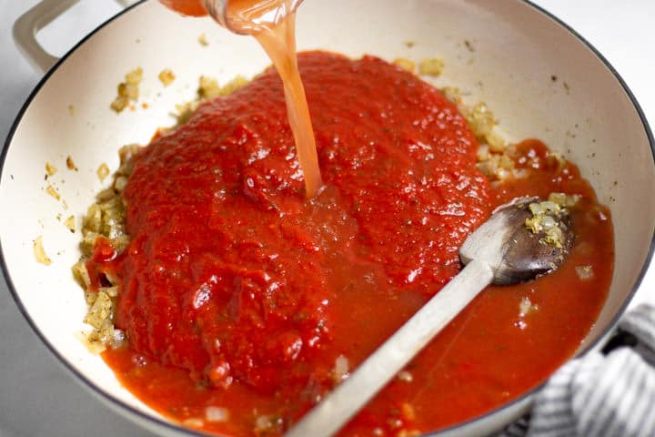 Large white saute pan with with red pasta sauce in it and water being poured into it 