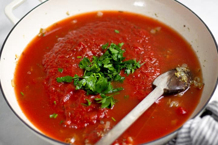 Large white saute pan with tomato sauce and parsley in it 