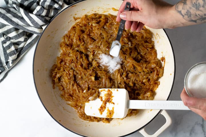 Large white pan filled with caramelized onions with sugar being added