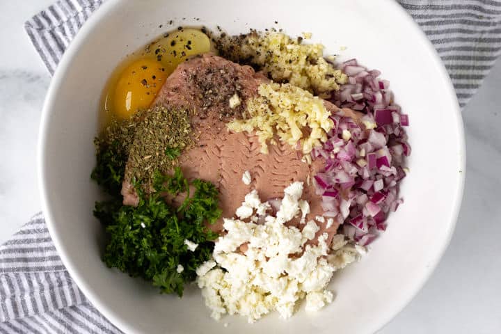 Large white bowl filled with ingredients to make Greek turkey burgers