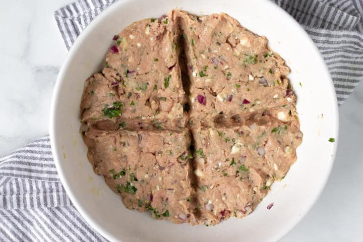 Large white bowl filled with ingredients to make Greek turkey burgers