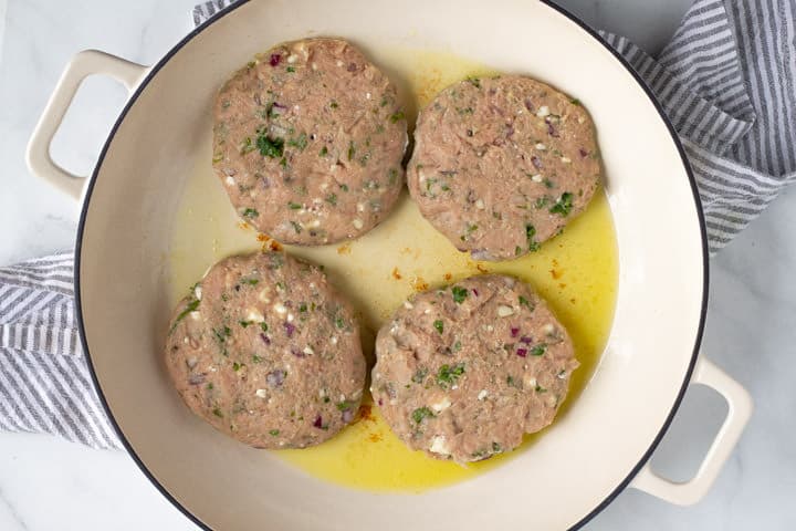 Large saute pan filled with olive oil and Greek turkey burgers