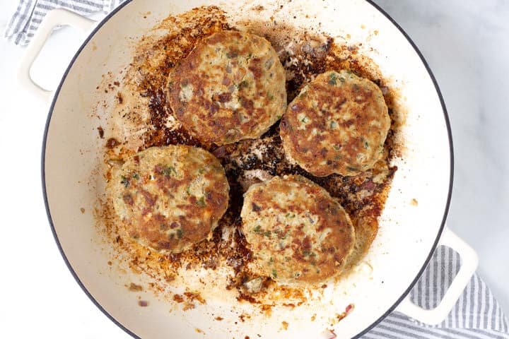 Large saute pan filled with olive oil and Greek turkey burgers