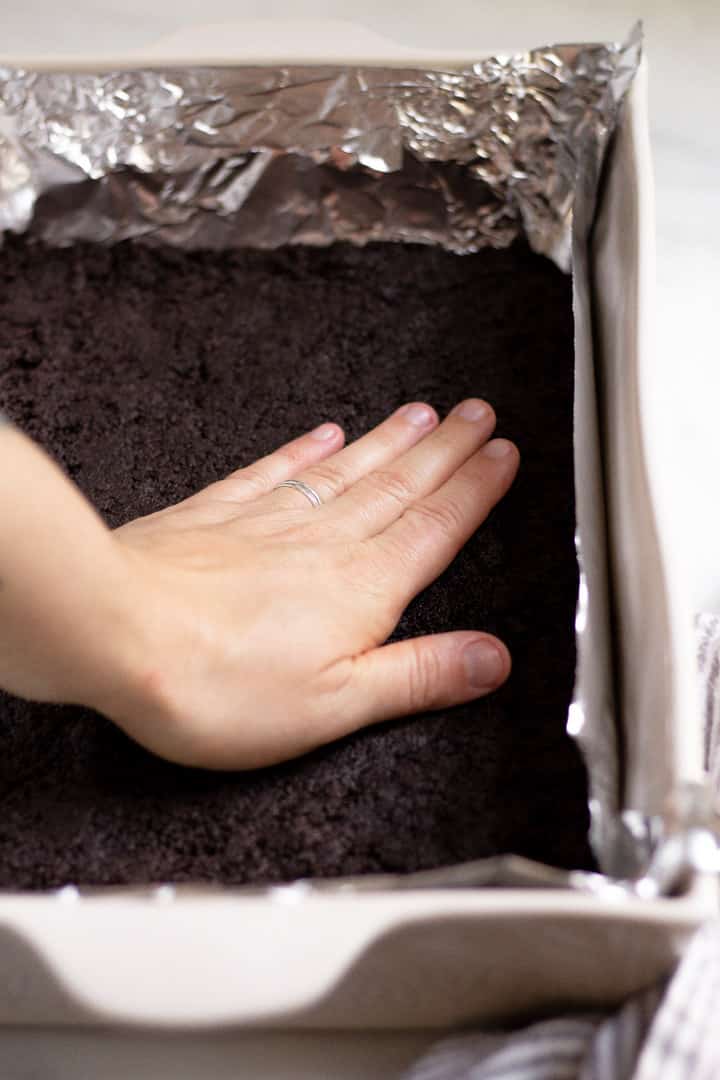 A hand pressing oreo crust into the bottom of a 9x13 inch pan