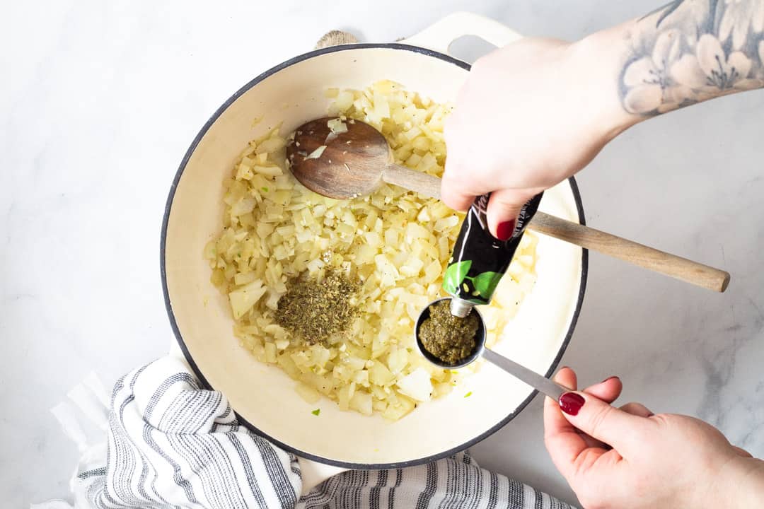 Large white pot filled with onions and oregano with vegan pesto being added