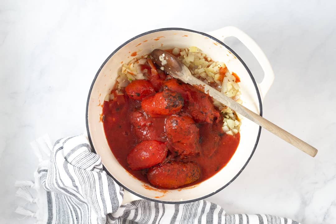 Large white pot filled with tomatoes onions and garlic for tomato soup