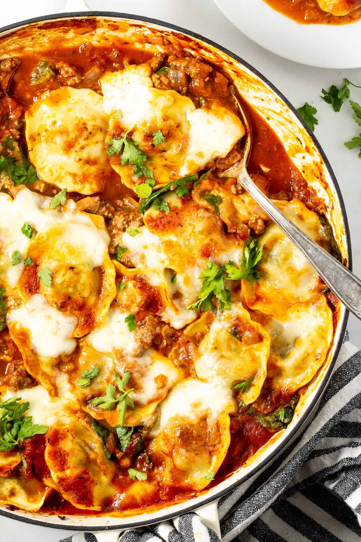 Overhead shot of a pan of baked ravioli garnished with fresh chopped parsley