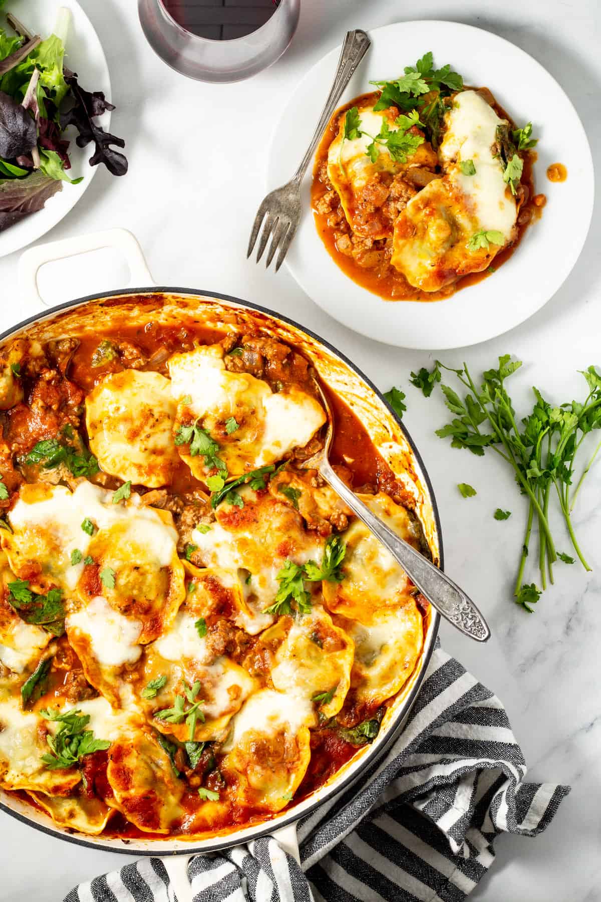 Overhead shot of a pan of baked ravioli with white plate next to it with ravioli dished up on it