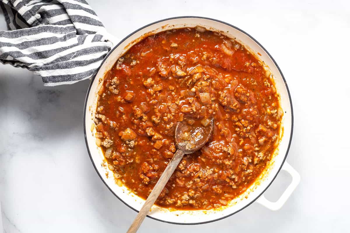 Large white saute pan filled with spaghetti sauce and ground sausage