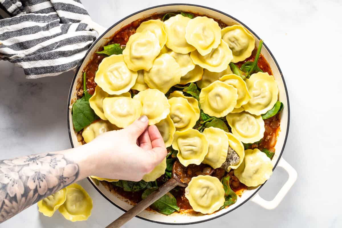Large white saute pan filled with spaghetti sauce spinach and round ravioli