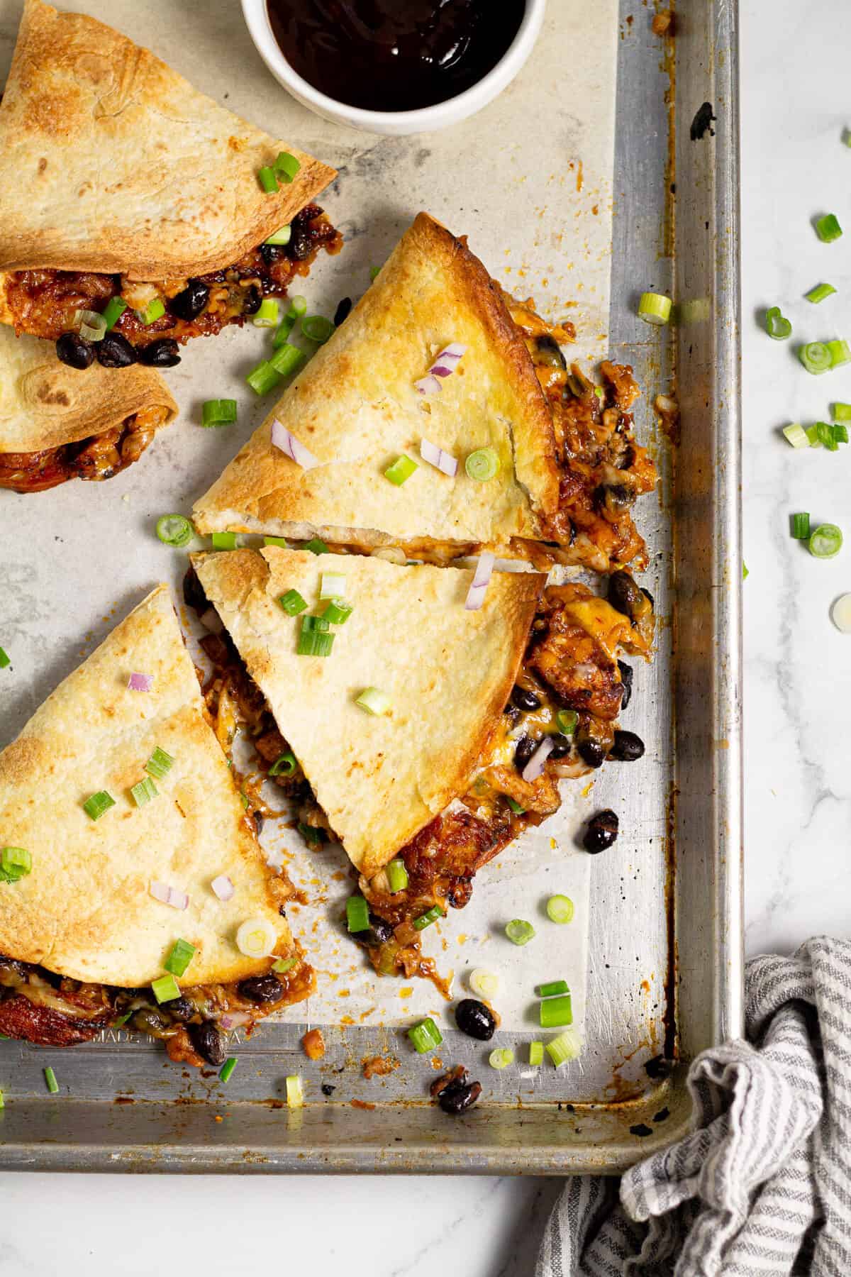 Overhead shot of a sheet pan of barbecue chicken quesadillas garnished with green onion