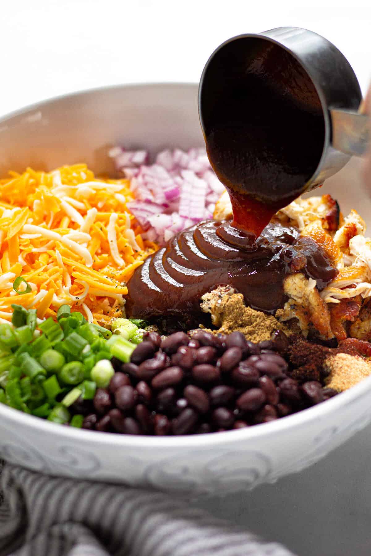 BBQ sauce being poured into a bowl filled with ingredients to make barbecue chicken quesadillas