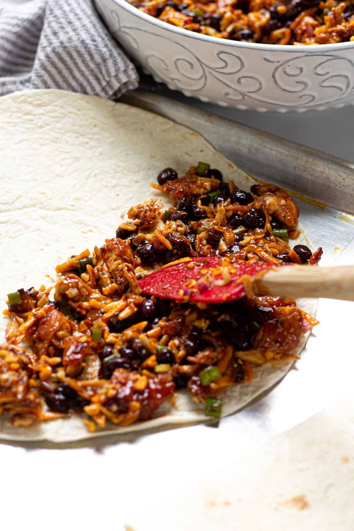 Chicken cheese and BBQ sauce being spread over a flour tortilla on a baking sheet