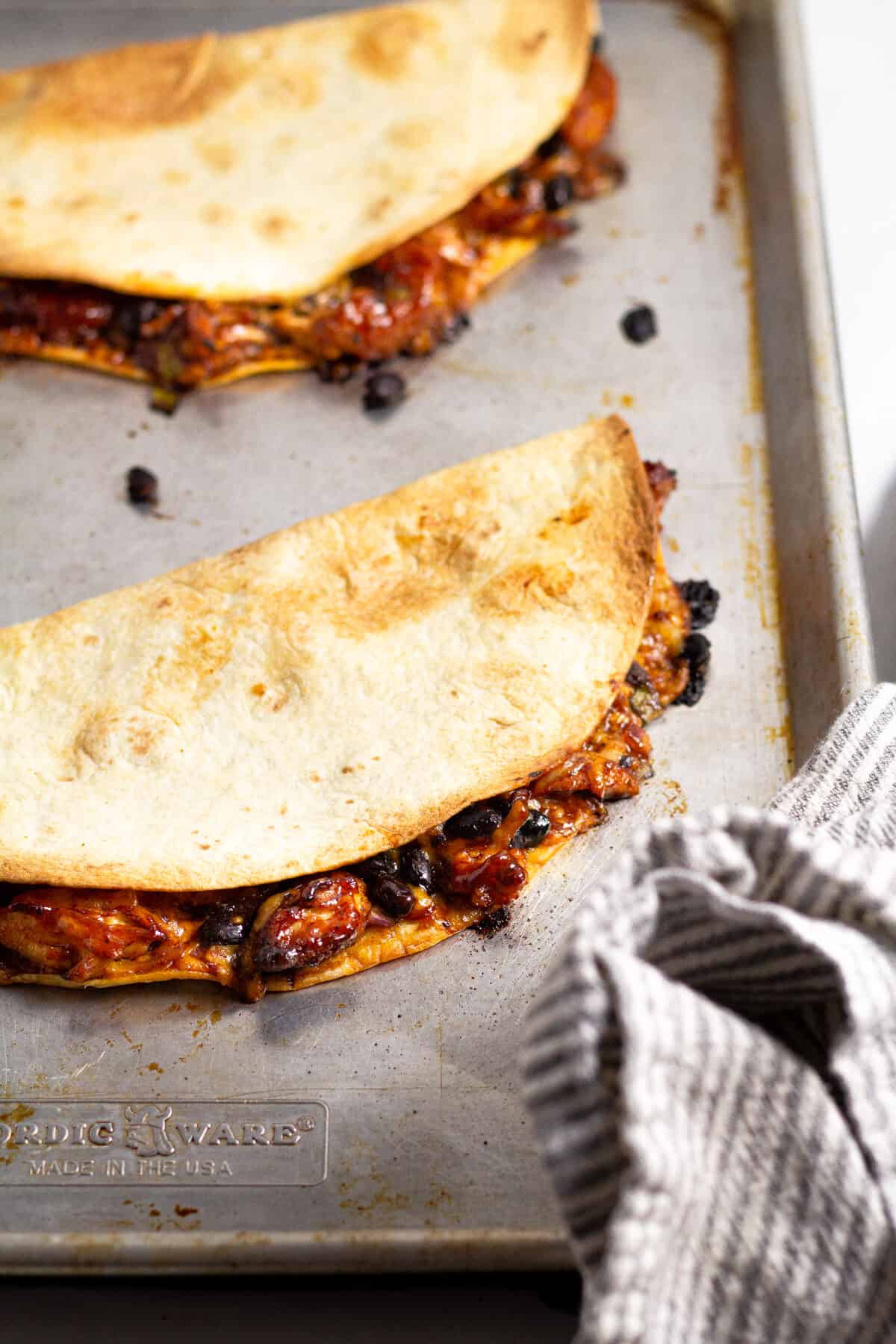 Close up shot of a sheet pan with baked chicken quesadillas on it