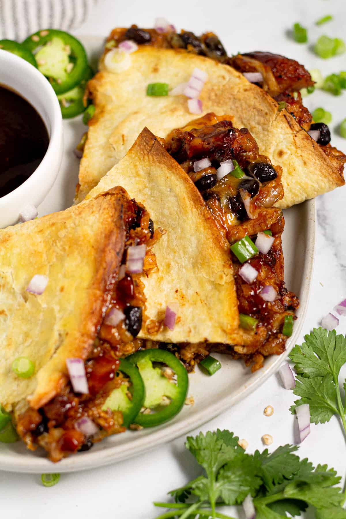 Close up shot of a plate of barbecue chicken quesadillas garnished with green onion