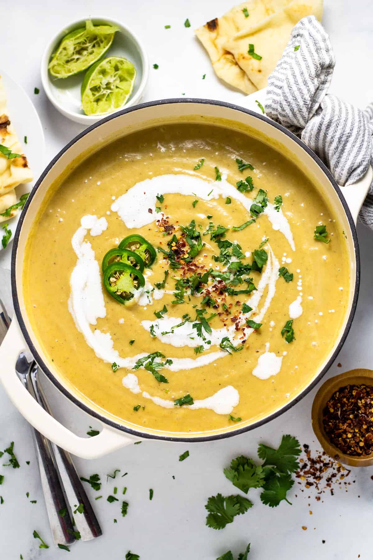 Large white pot filled with creamy vegan cauliflower soup garnished with coconut milk and fresh chopped cilantro 