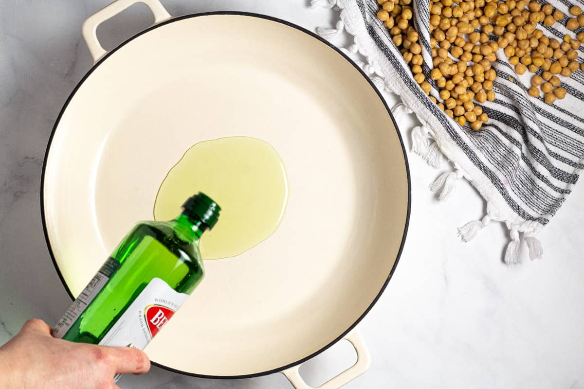 Large white saute pan with olive oil being poured into it