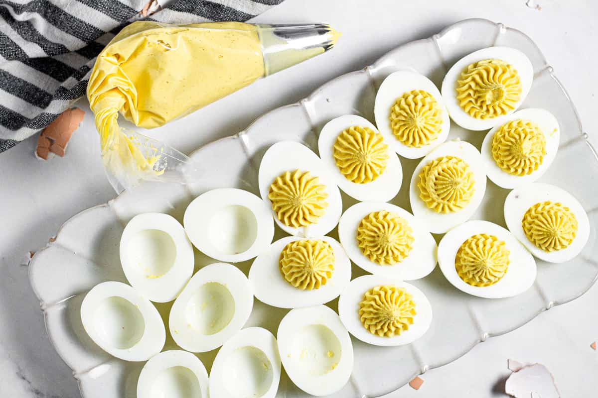 White platter filled with deviled eggs with a piping bag filled with yolks next to it