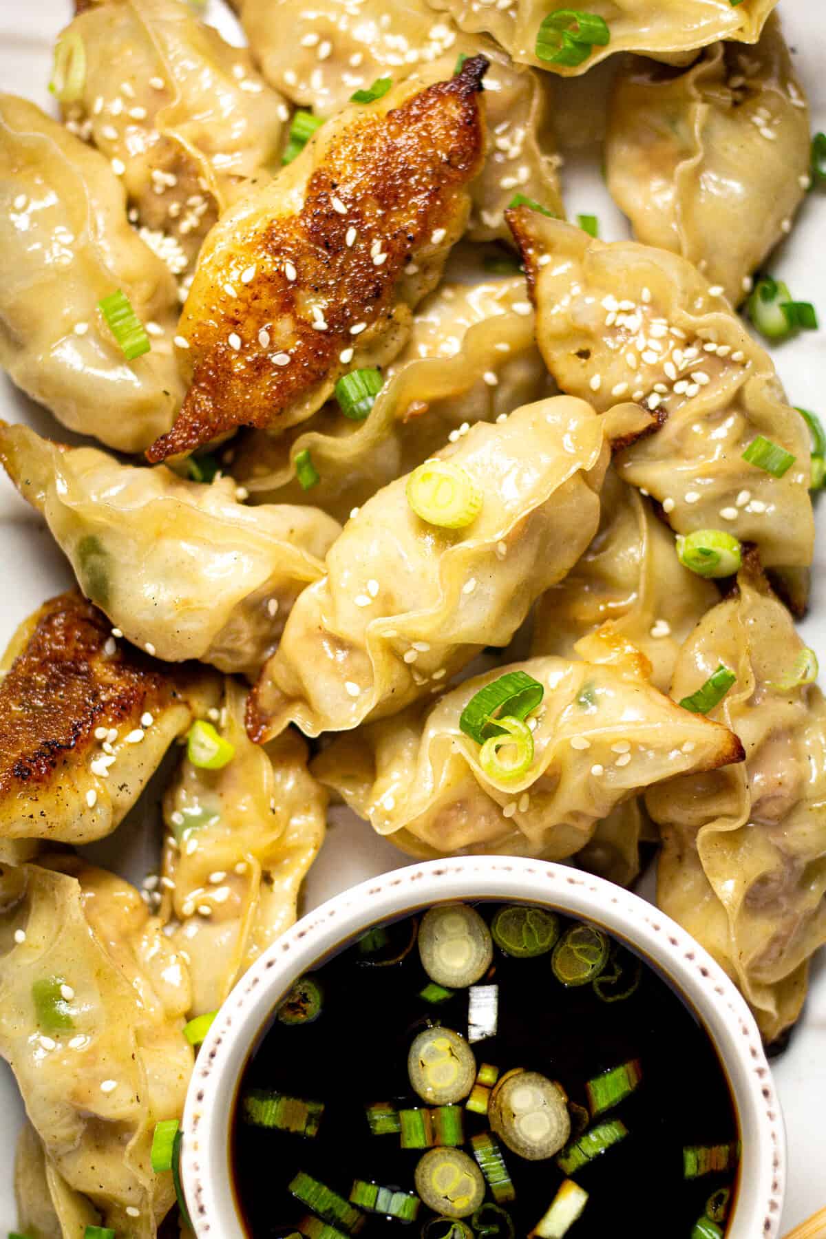 Overhead shot of a platter filled with pork dumplings garnished with green onions and sesame seeds