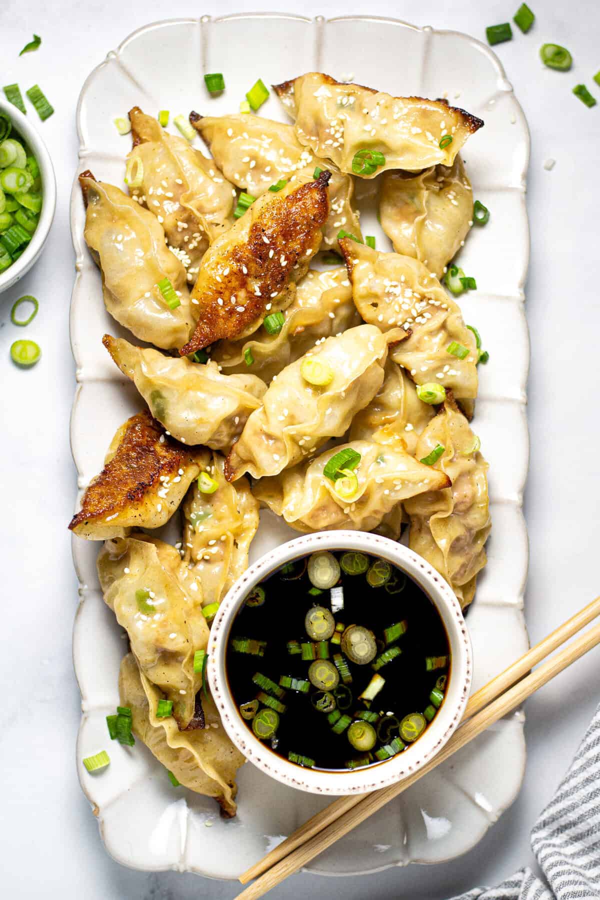 Large white platter filled with homemade pork dumplings garnished with sliced green onions