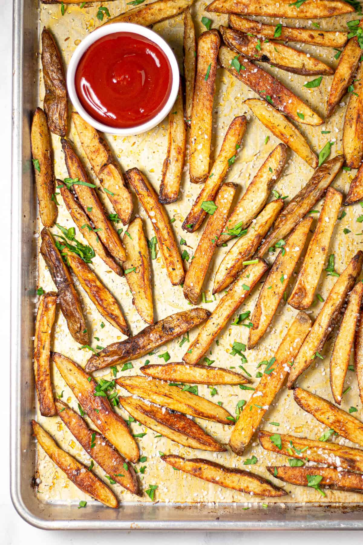 Overhead shot of a baking sheet filled with baked fries and ketchup