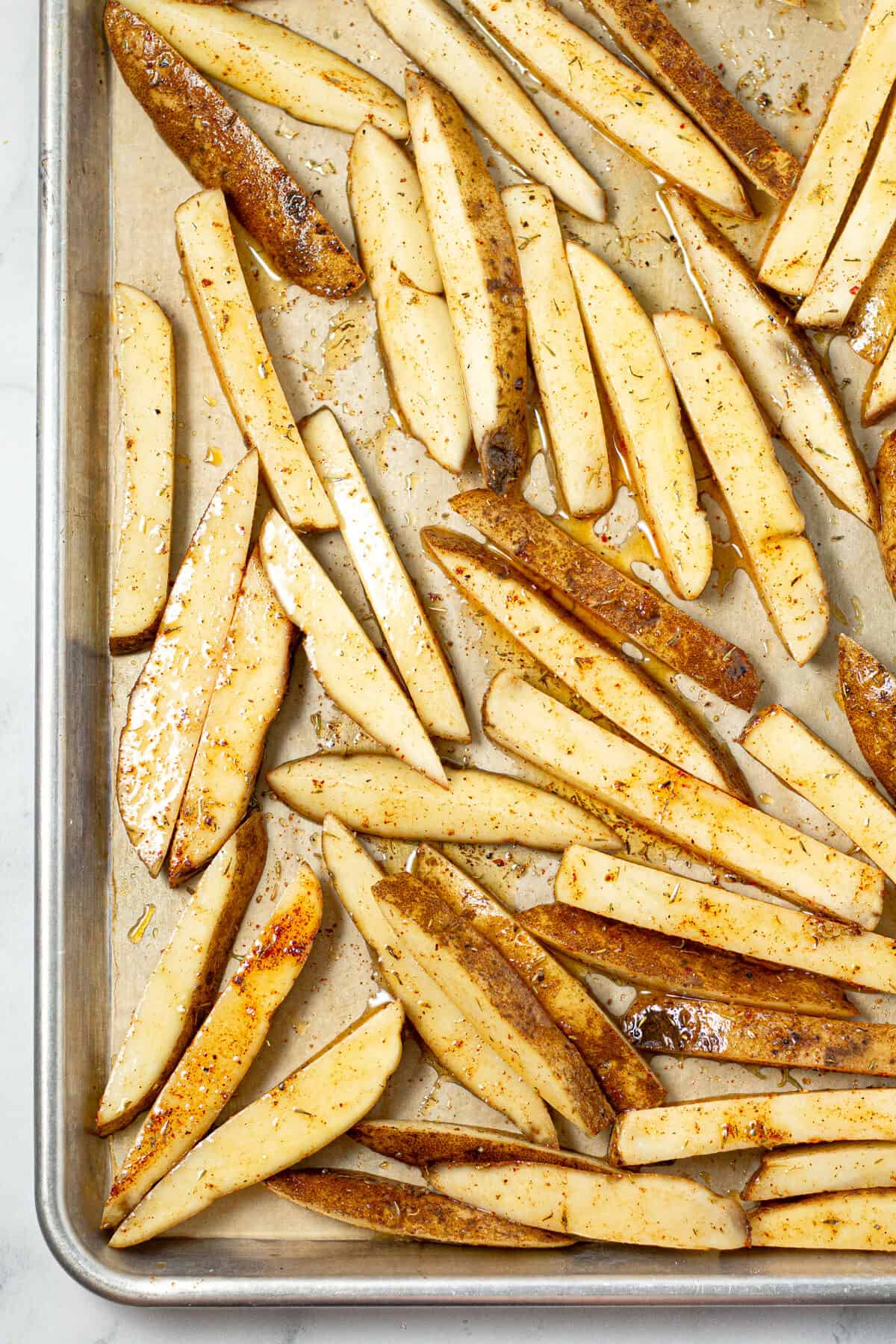 Parchment lined baking sheet with fresh cut French fries ready for the oven 