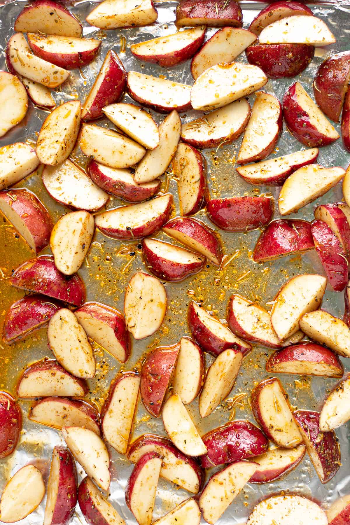 Potato wedges on an aluminum foil lined baking sheet tossed in olive oil and herbs