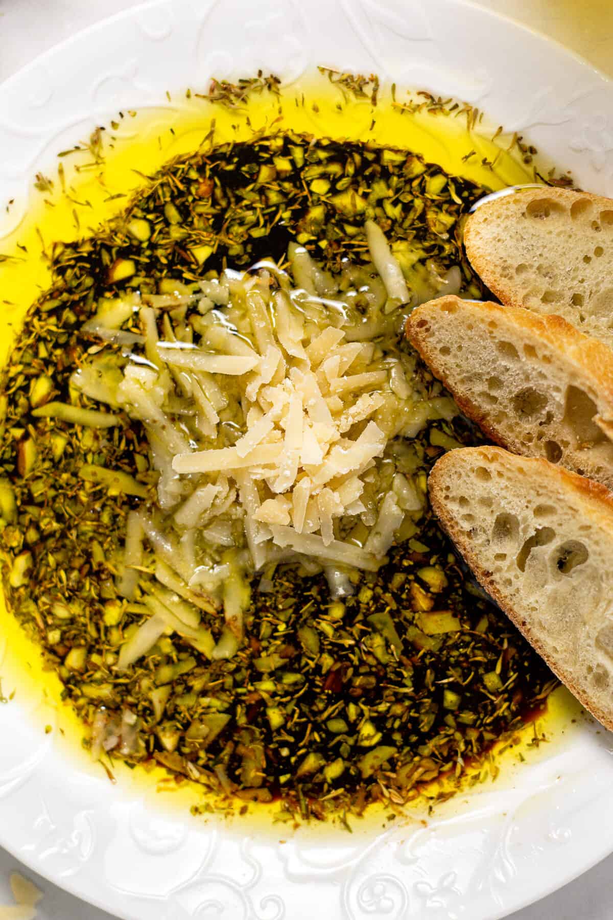 Overhead shot of a plate filled with olive oil and balsamic vinegar dip with Parmesan cheese and herbs