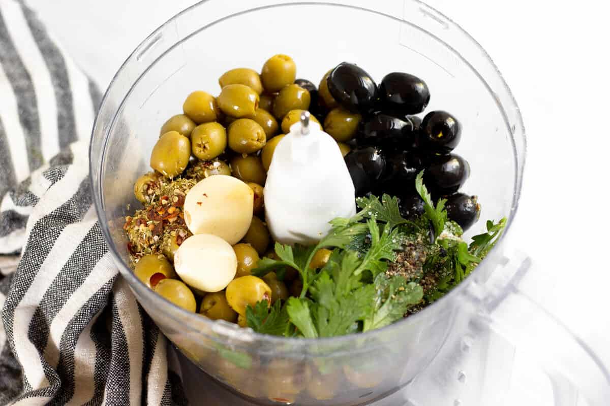 Food processor filled with ingredients to make olive tapenade