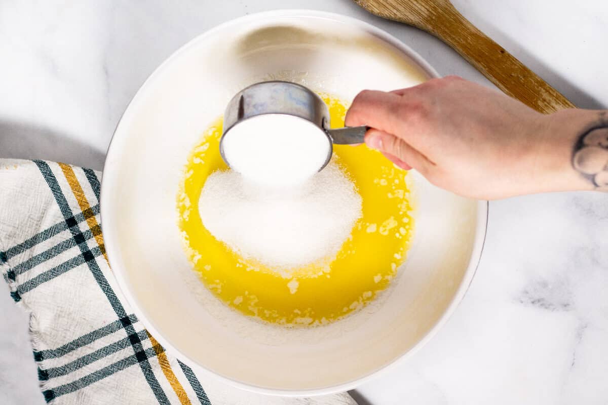 Large white bowl filled with melted butter with granulated sugar being poured into it