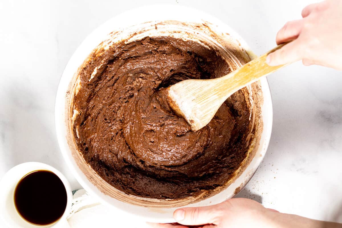 Large white bowl with brownie batter in it and a hand stirring the batter with a wooden spoon 