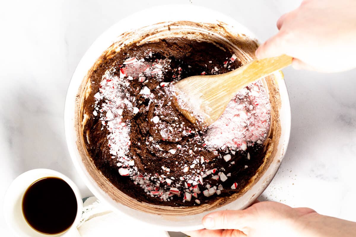 Large white bowl with brownie batter in it and a hand stirring the batter with a wooden spoon 