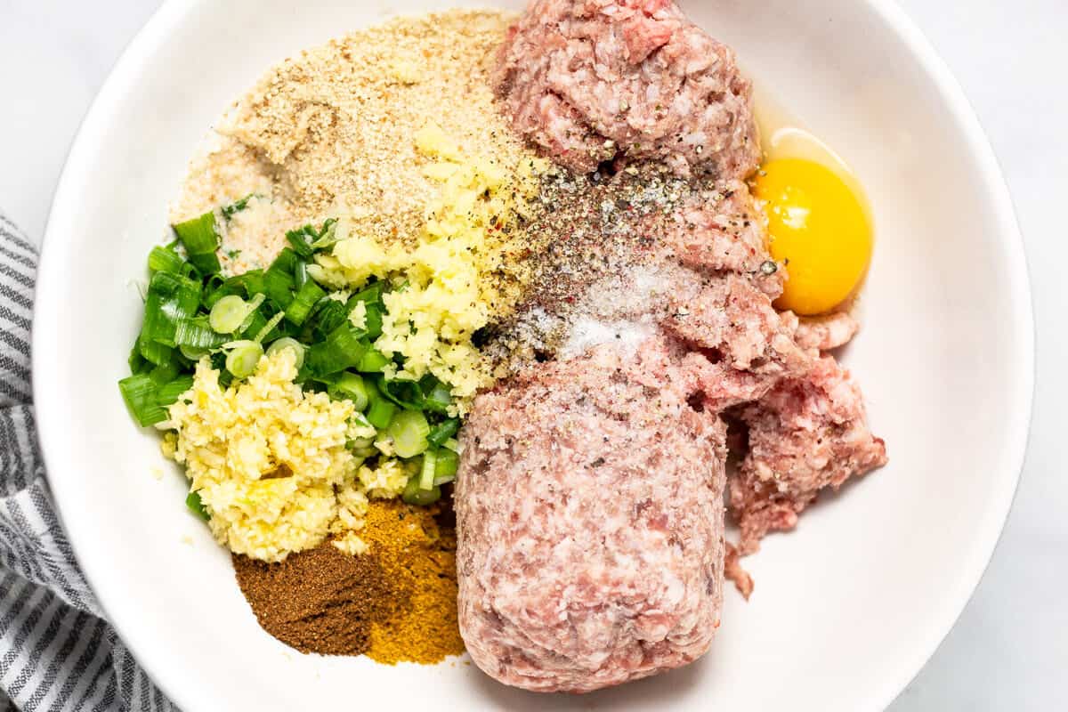 White bowl filled with the ingredients to make pork meatballs
