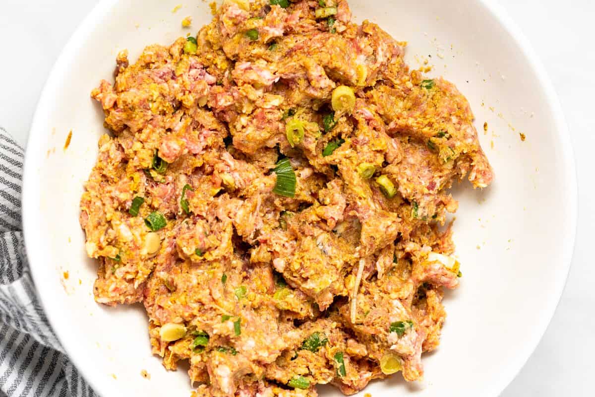 White bowl filled with the ingredients mixed together to make pork meatballs