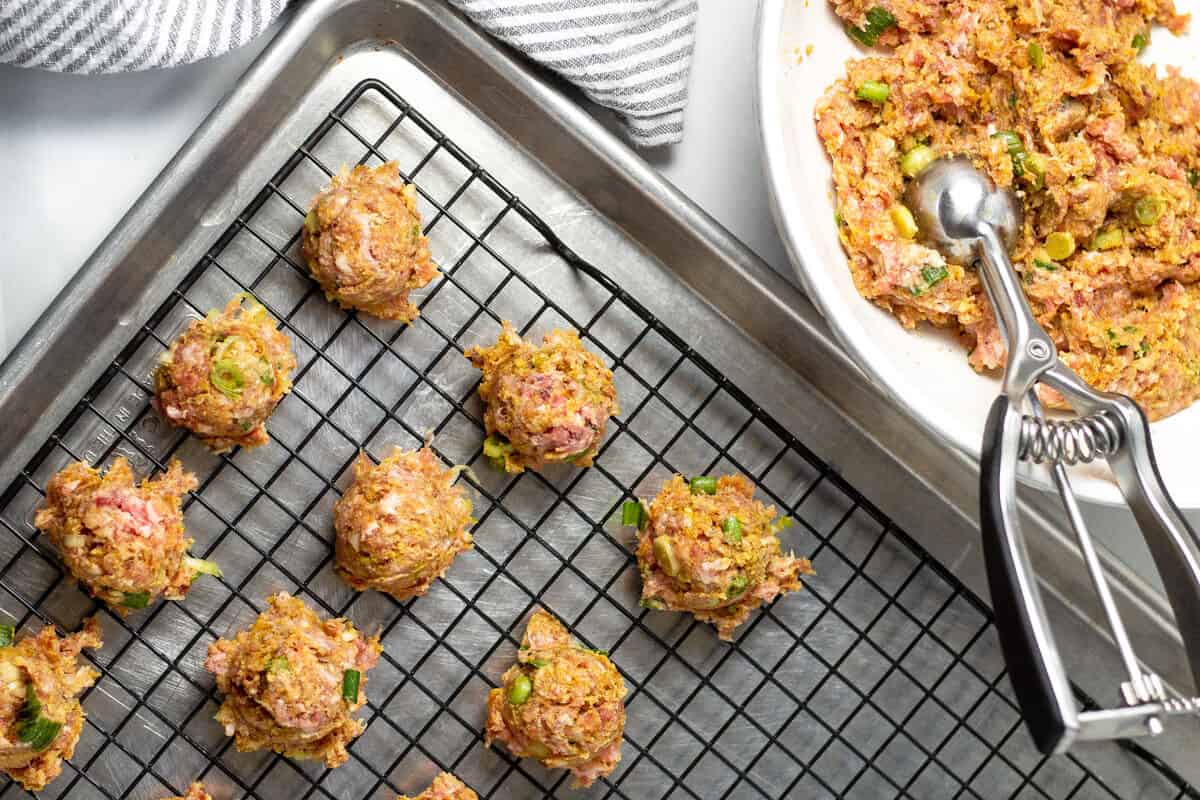 Baking sheet with a cooling rack on top and a cookie scoop scooping meatballs