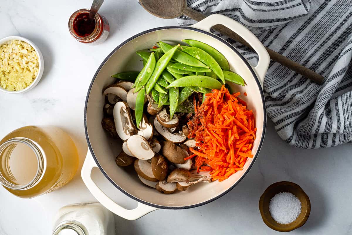 Overhead shot of a white dutch oven filled with ingredients to make vegan curry ramen noodles.