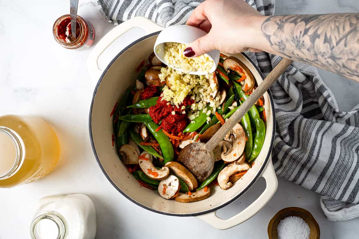 Overhead shot of a white dutch oven with garlic being added to vegetables.