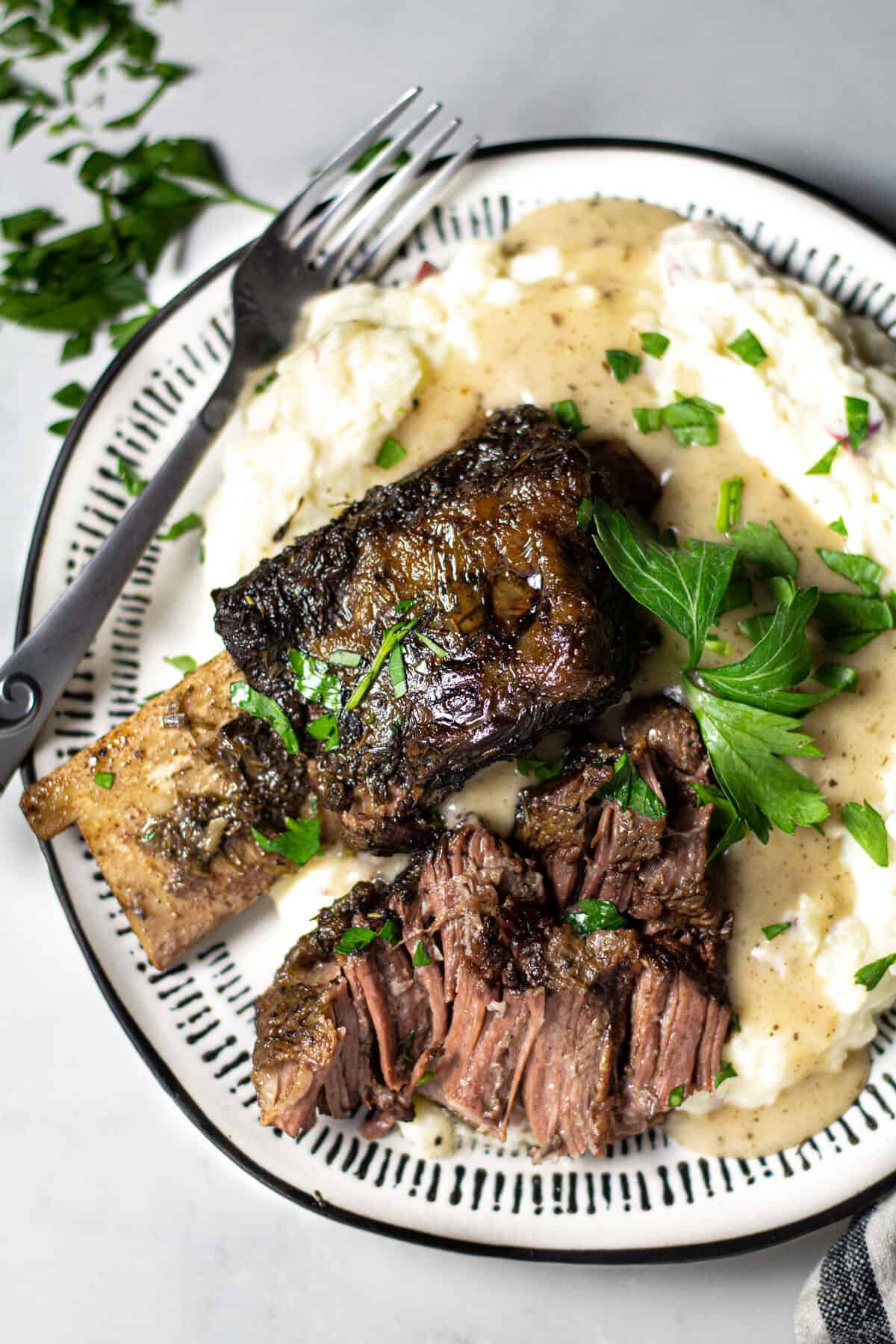 Overhead shot of a plate filled with short ribs and homemade mashed potatoes garnished with parsley 