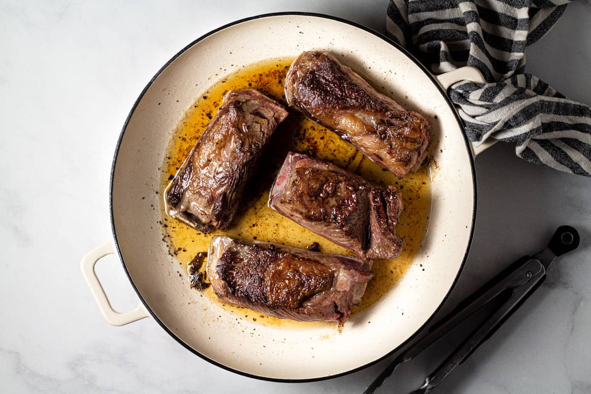 Large pot filled with seared short ribs on a marble counter top 